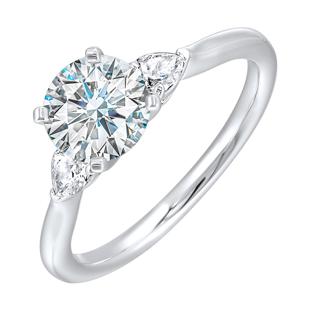 Stunning engagement ring features a round brilliant cut diamond in the center of a three stone setting,  adorned on either side by a smaller pear diamond set on the tapered shank.